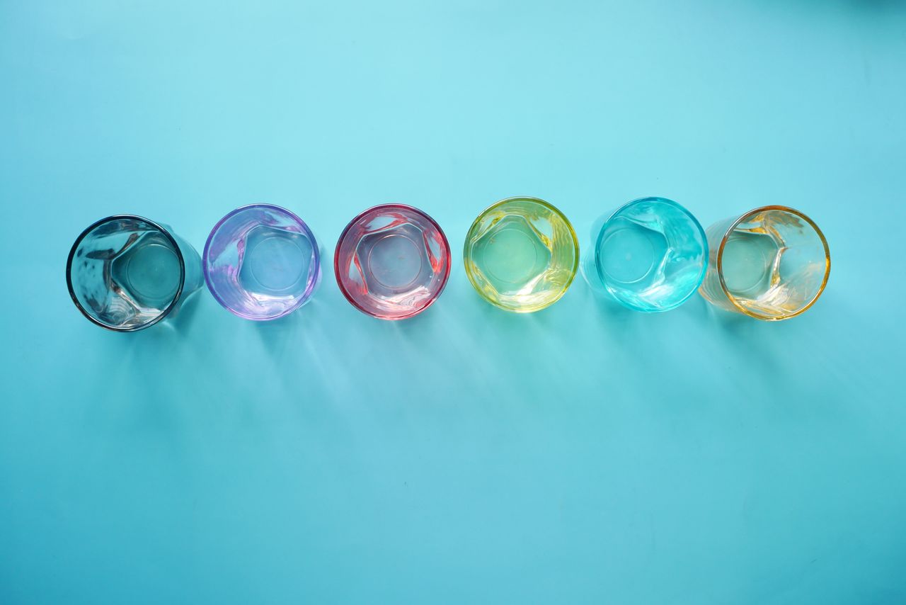 Top view of six colorful drinking glasses arranged on a blue surface.