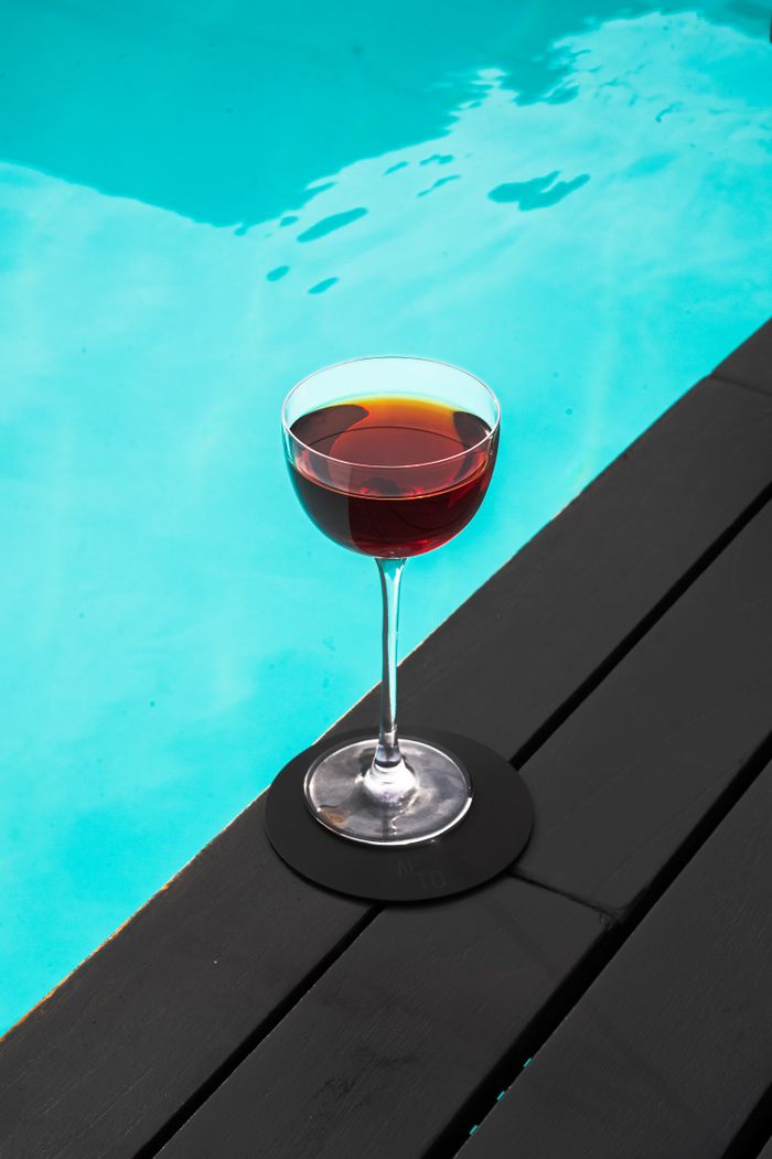 A refined wine glass with red liquid sits on a poolside deck, perfect for summer relaxation.