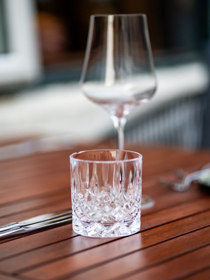 Close-up of a crystal glass and wine glass setting on a wooden table outdoors.