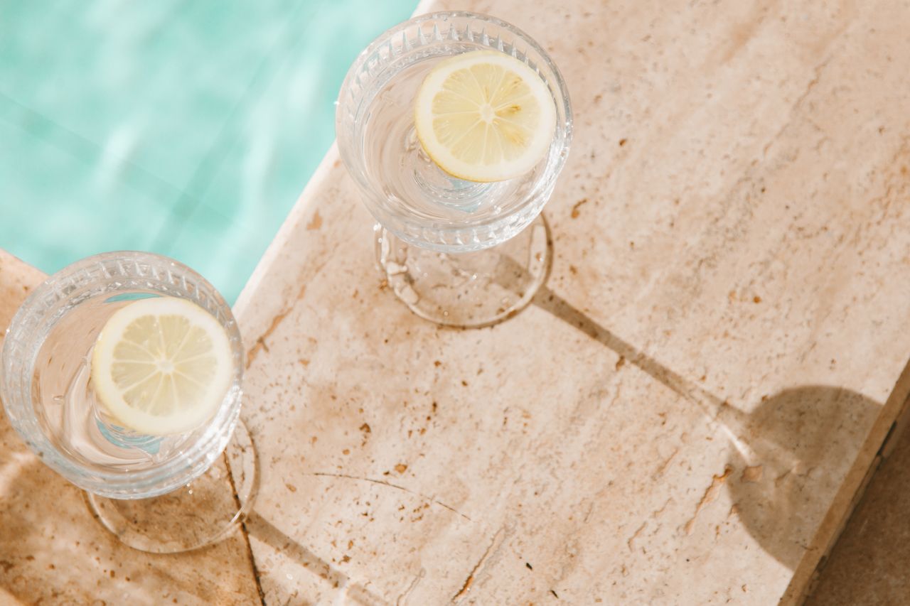 Two lemon water glasses on a sunlit concrete surface by a pool, perfect for summer vibes.