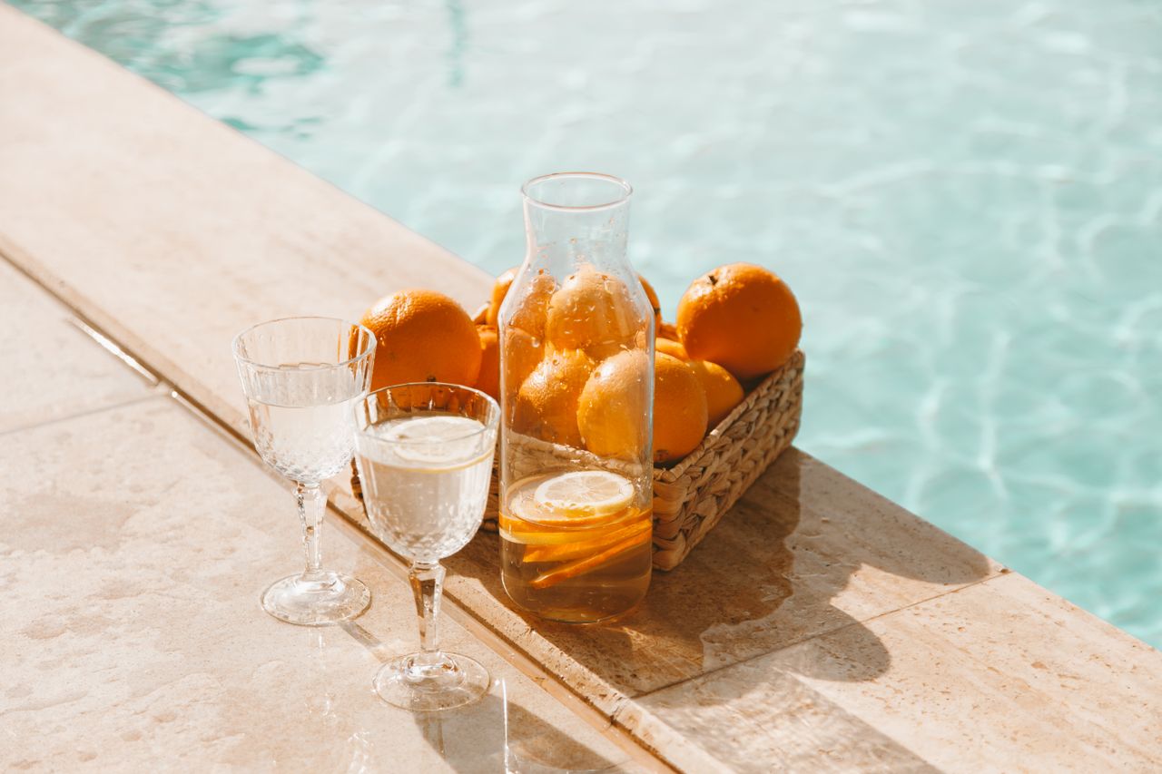 Decorative lemon water with fresh oranges by a sunlit poolside, perfect for summer vibes.