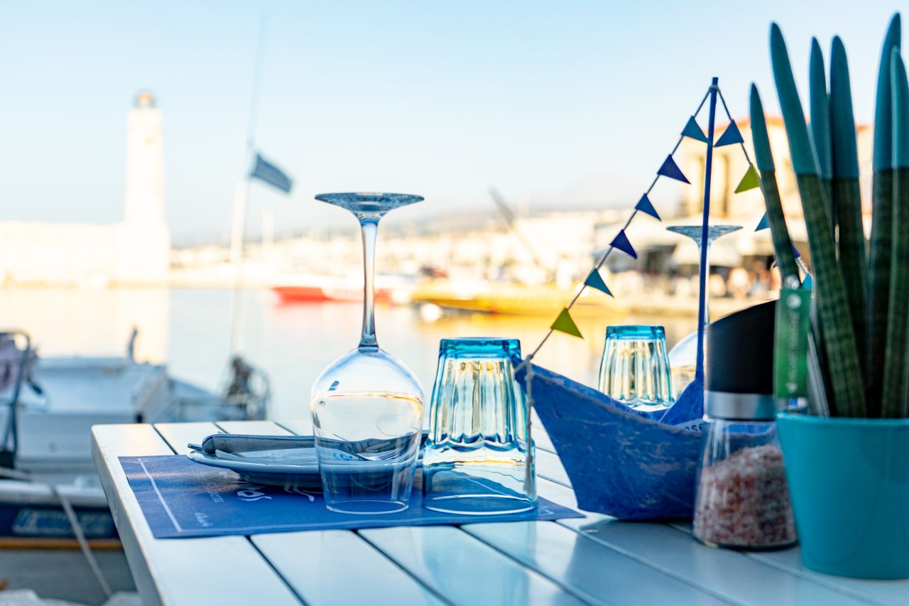 Services A picturesque outdoor dining setup with glasses and a plant by a marina during daytime.