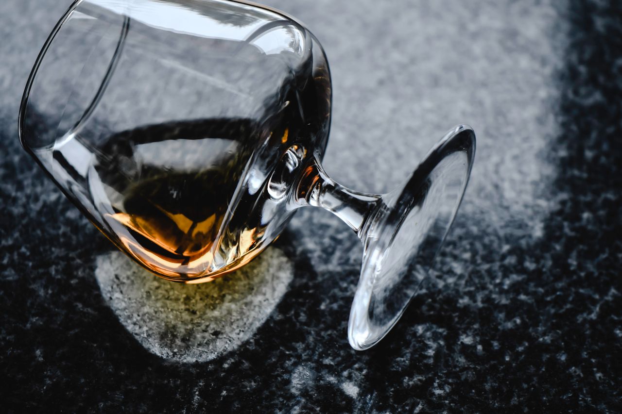 A delicate whiskey glass with liquor spills gracefully on a polished granite surface.
